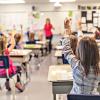 Children sitting at desks in a classroom and raising their hands