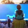 Child sitting on his father's neck watching a movie in the open air