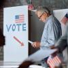 Man examines a piece of paper in front of a booth labeled with the American flag and the word "vote"
