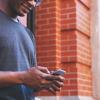 Person leans against brick wall, checking smartphone