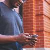 Person leans against brick wall, checking smartphone