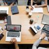 Team sits at table with laptops, notebooks
