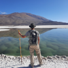 Brian Hynek holding a walking stick on the shore of a lagoon