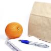 Brown paper bag with notebook, pen and orange