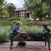 two students sit on a bench on campus, talking