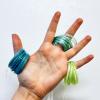 Hand holds three coils of thread in blue, green and neon green