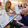 A CU engineering student helps a patient at the paper airplanes table during STEAM camp at Children's Hospital.