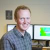 Portrait of CU student Matthew Hurst in front of monitors displaying his computer modeling graphics