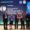 Dan Baker holds a plaque and poses for a group photo on a stage.