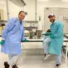 Tobias Niederwieser and Luis Zea pose by two cases on a table in a lab