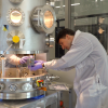 Man wearing a lab coat and gloves makes adjustments inside a large metal chamber