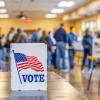 Sign with American flag and the word "Vote" sits out on a table while people mill around in the background