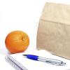 Brown-bag lunch, notebook, pen and an orange
