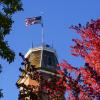 Flag flying atop Old Main building framed in red autumn leaves