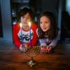 Two Asian American children look at a lit menorah