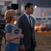 Man and women stand side-by-side with camera in the background. Woman carries a clipboard labeled "NASA"