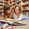 two young girls lying on the floor reading a book together
