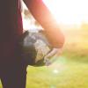 Woman stands in field holding globe in hand