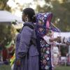 Indigenous woman wearing a baby in a carrier on her back while another woman holds the baby's hands