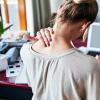 person rubbing neck while sitting at desk