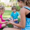 A boy, girl and babysitter sit on carpet and play.