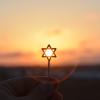 Person holds a small Jewish star in front of a setting sun
