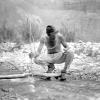 Man holding pole crouches in stream