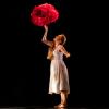 A dancer in a white flowing dress on stage with large red flower shapes.