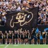 Student runs down sideline with a giant CU flag during a football game