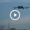 A drone in the sky, mid-flight, with an overlay image of a play button.