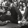 Martin Luther King Jr. in a car and shaking hands with people standing nearby