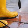 Person wearing yellow rubber boots and power washing the ground