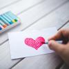 person drawing a red heart on a piece of paper