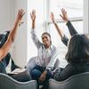 Professional women sit in a circle with hands raised