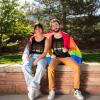 Students sitting outdoors on campus with a pride flag draped around their shoulders