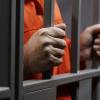 prisoner in orange jump suit grasping prison bars