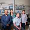 Two women and two men pose for a photo in front of a lab bench