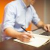 Researcher sits at computer, writes in notebook