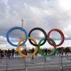 Statue of five Olympic rings in foreground with plaza and Eiffel Tower in the background