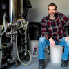 Man in flannel shirt wearing safety glasses sits next to equipment with lots of tubes