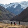 People walking toward a snow-covered mountain through a dry river bed of rocks.