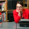 Artist Sheryl Oring, dressed in red white and blue, sits at a desk in front of her vintage typewriters.