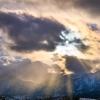 Sun peaks through clouds over snow-covered Flatirons