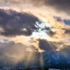 Sun peaking through clouds over snow-covered mountains near campus