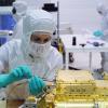 Woman in clean room bunny suit and wearing a mask uses a tool to make an adjustment on a gold instrument