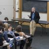A professor stands in front of a class, taking notes in an auditorium