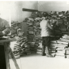 Black and white image of men looking through massive piles of books