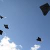 A number of graduation caps are suspended in air with a blue-sky backdrop.