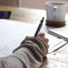 Person writing on paper with coffee mug in the background