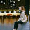 Woman sits in an airport while wearing a mask.
